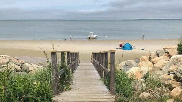 Une promenade en bois menant à une plage où se trouvent un bateau et une tente.
