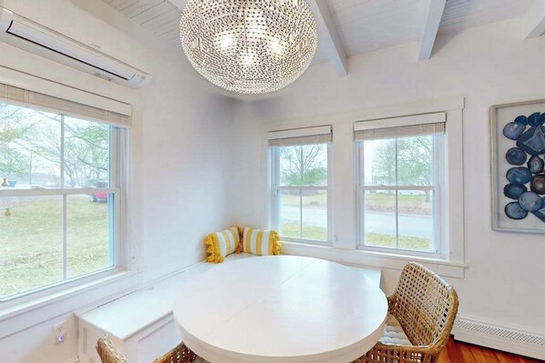 A room with a round white table, wicker chairs, a large woven light fixture, and a window with blinds.