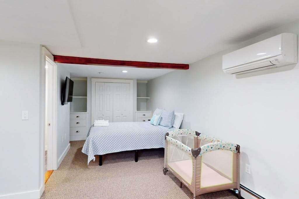 A bedroom with a bed, a crib, a wardrobe, and an air conditioning unit.