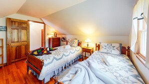 Une chambre avec deux lits, un plancher en bois, une porte, une table de chevet, une lampe et une fenêtre.