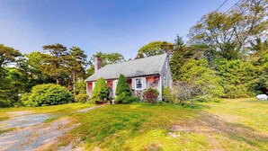 Une maison avec un toit en pente, entourée d’une pelouse bien entretenue et de divers arbres.