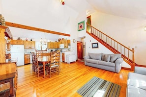 A spacious living area with a wooden dining table, a sofa, and a staircase. - Delightful, dog-friendly home with private deck, grill, outdoor dining & WiFi (Brewster)