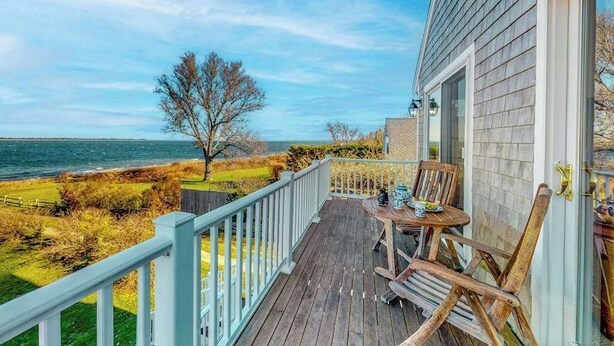A wooden deck with a table and chairs, overlooking a grassy area and the sea. - Private water access & stunning views (Barnstable)
