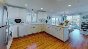 A modern kitchen with white cabinetry, a wooden floor, and a dining area with a view. - Private water access & stunning views (Barnstable)