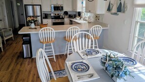 A modern kitchen with white cabinetry, a central island with bar stools, and a dining area with blue and white plates. - Private water access & stunning views (Barnstable)