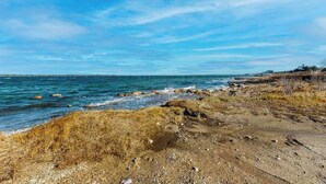 A coastal landscape with a rocky shoreline, a clear sky, and a distant view of a small settlement. - Private water access & stunning views (Barnstable)