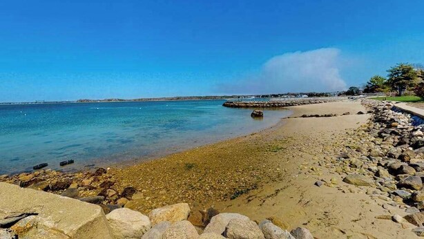 Una platja amb aigua cristal·lina, un litoral rocos i un moll allunyat.