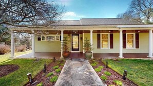 A two-story house with a covered porch, a stone pathway leading to the entrance, and potted plants. - Wonderful waterfront getaway with furnished deck, pond access, kayaks & WiFi (Cotuit)