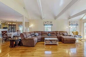 Ein großzügiger Wohnraum mit einer großen Eckcouch, Holzboden und einem Essbereich mit Tisch und Stühlen.