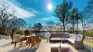 A deck with outdoor furniture, a white railing, and a view of trees and water. - Wonderful waterfront getaway with furnished deck, pond access, kayaks & WiFi (Cotuit)