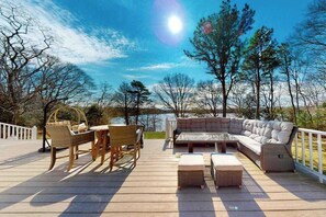 Eine Terrasse mit Gartenmöbeln, einem weißen Geländer und Blick auf Bäume und Wasser.