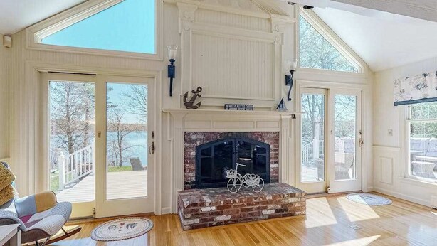 A spacious room with a fireplace, large windows, and a wooden floor. - Wonderful waterfront getaway with furnished deck, pond access, kayaks & WiFi (Cotuit)