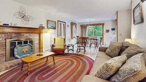 Een woonkamer met een open haard, een bank, een eettafel en stoelen.