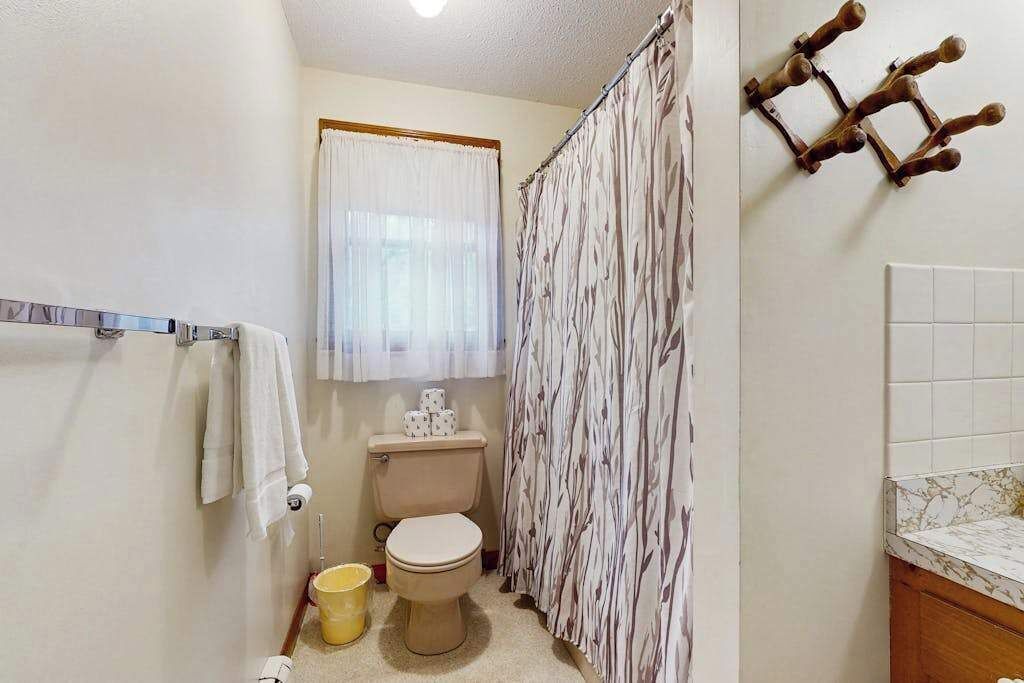 Une salle de bain équipée de toilettes, d’un rideau de douche, d’un porte-serviettes et d’un comptoir en marbre.