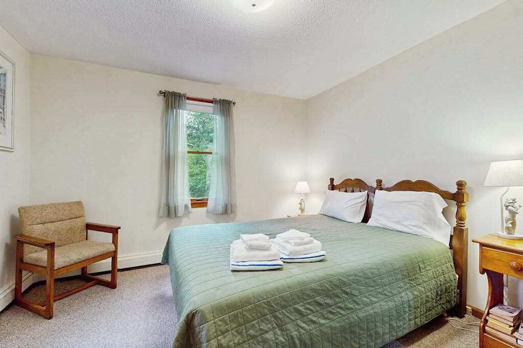 A bedroom with a bed, a chair, a nightstand, and a window with curtains.