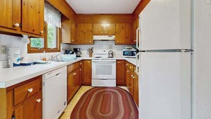 Een kleine keuken met houten kastjes, een witte koelkast, een fornuis en een magnetron.