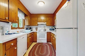 A compact kitchen with wooden cabinets, a white refrigerator, a stove, and a microwave.