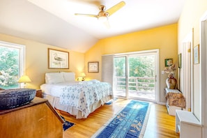 A bedroom with a bed, a ceiling fan, a large window, and a view of greenery outside.