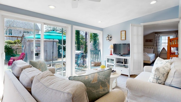 A living room with a sofa, television, and a view of the outside. - Classic Cape Cod home with Patio and Firepit - Walk to the Beach (Dennis Port)