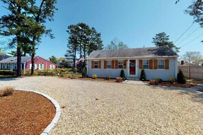 A single-story house with a front porch, a driveway, and a well-maintained lawn. - Classic Cape Cod home with Patio and Firepit - Walk to the Beach (Dennis Port)