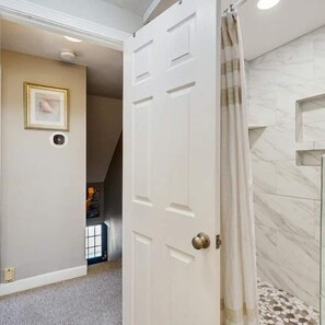Una habitación con una puerta que da a un baño con ducha y piso de baldosas.