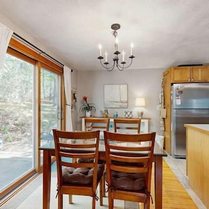 A dining area with a table, chairs, a chandelier, a refrigerator, and a window with curtains. - Dog-friendly Bournes Pond home minutes to downtown Falmouth with grill (East Falmouth)