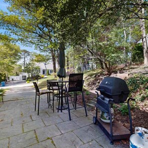 Eine Terrassengruppe im Freien mit Grill, Tisch, Stühlen und Sonnenschirm.