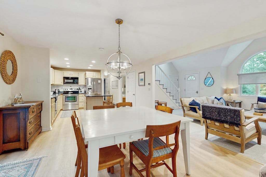 A spacious living area with a dining table, wooden chairs, a sofa, and a staircase leading to an upper level.