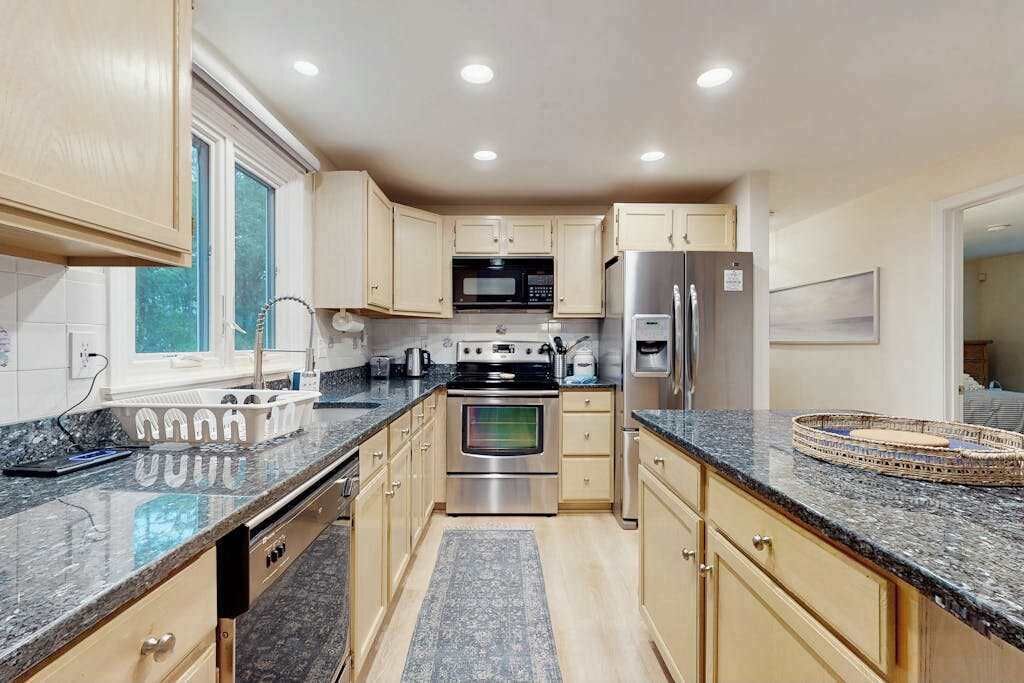 A modern kitchen with granite countertops, stainless steel appliances, and light wood cabinets.