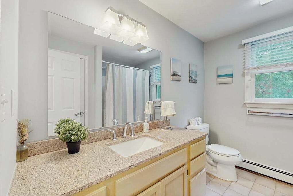 Une salle de bain avec un grand miroir, un lavabo, des toilettes et une fenêtre avec des stores.