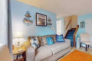 A living room with a sofa, pillows, a lamp, and wall decorations. - Nautical oceanside duplex with fast WiFi & central AC - walk to Sea Street Beach (Dennis Port)