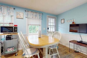 A dining area with a wooden table, white chairs, a microwave, a toaster, and a television. - Nautical oceanside duplex with fast WiFi & central AC - walk to Sea Street Beach (Dennis Port)