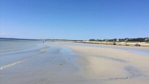 Una spiaggia con cielo sereno, acqua calma e edifici in lontananza.