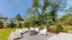 An outdoor patio with white chairs, a stone fire pit, and a table. - Lovely dog-friendly home w/ fireplace, central AC, full kitchen, & washer/dryer (Dennis)