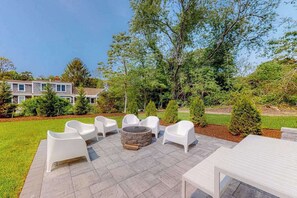 An outdoor patio with white chairs, a stone fire pit, and a table. - Lovely dog-friendly home w/ fireplace, central AC, full kitchen, & washer/dryer (Dennis)