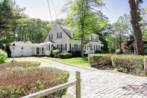 A two-story house with a porch, surrounded by a well-maintained garden and trees. - Coastal Retreat w/ Sunroom & Yard – Walk to Private Beach & Harwich Port (Harwich Port)