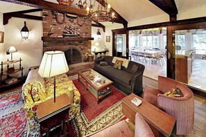 A cozy living room with a fireplace, a sofa, a coffee table, and a dining area visible through glass doors. - Coastal Retreat w/ Sunroom & Yard – Walk to Private Beach & Harwich Port (Harwich Port)
