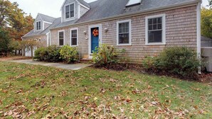 A two-story house with a blue front door, a small porch, and a well-maintained lawn. - Quaint home w/ large backyard, outdoor shower & private grill near Katama Bay (Edgartown)