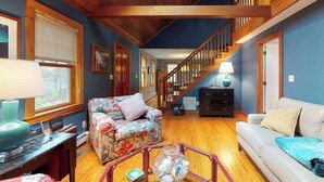 A spacious living room with a wooden staircase, a sofa, a coffee table, and a lamp. - Quaint home w/ large backyard, outdoor shower & private grill near Katama Bay (Edgartown)