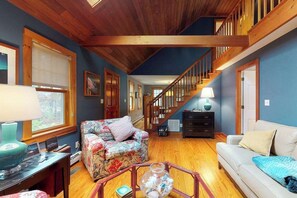 A spacious living room with a wooden staircase, a sofa, a coffee table, and a lamp. - Quaint home w/ large backyard, outdoor shower & private grill near Katama Bay (Edgartown)