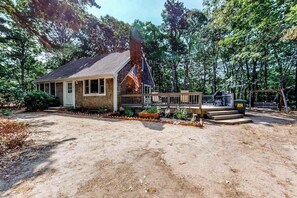 A rustic cabin with a wooden deck, surrounded by trees.