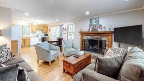 Ein Wohnzimmer mit Kamin, Fernseher und einer Küche im Hintergrund.