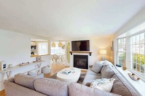 Ein modernes Wohnzimmer mit Kamin, Fernseher und großem Fenster.