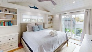 Ein Schlafzimmer mit Bett, Deckenventilator, Fenster und Blick ins Freie.