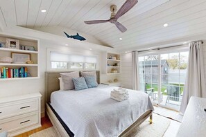 Ein Schlafzimmer mit Bett, Deckenventilator, Fenster und Blick ins Freie.