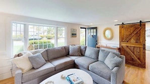 Ein Wohnzimmer mit einem grauen Ecksofa, einem weißen Couchtisch und einer Holztür im Scheunenstil.