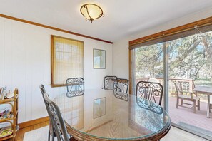 A dining area with a glass table, metal chairs, a wooden chair, a wicker chair, a ceiling light fixture, and a view of the outdoors.