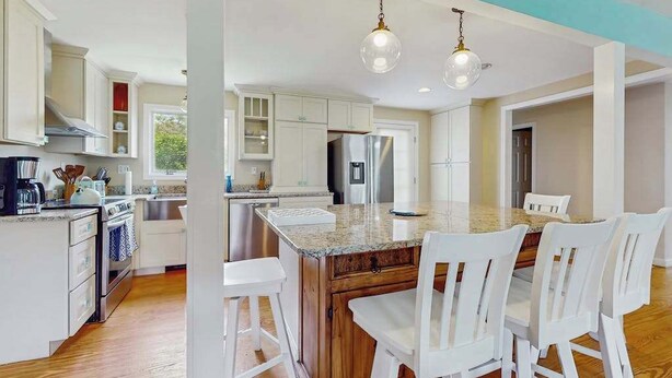 Una cocina moderna con armarios blancos, encimera de granito, electrodomésticos de acero inoxidable y una isla central con taburetes de bar.