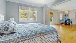 Un dormitorio con cama, ventana, puerta que da a un comedor y ventilador de techo.