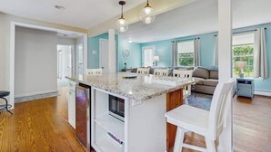 Una cocina moderna con una isla central, un comedor y una sala de estar con sofá y televisor.